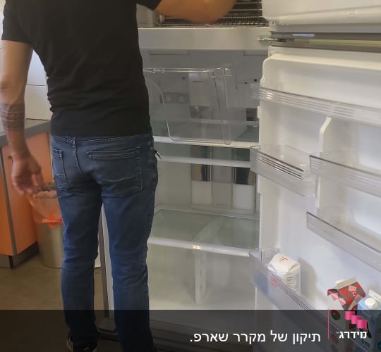 אדם מתקן מקרר פתוח עם מדפים ריקים